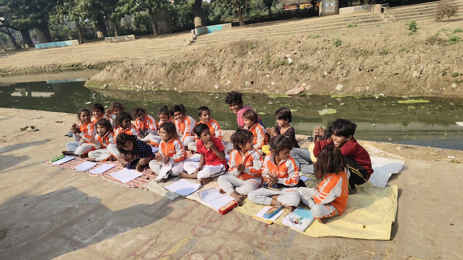 Children studying on mats beside the canal