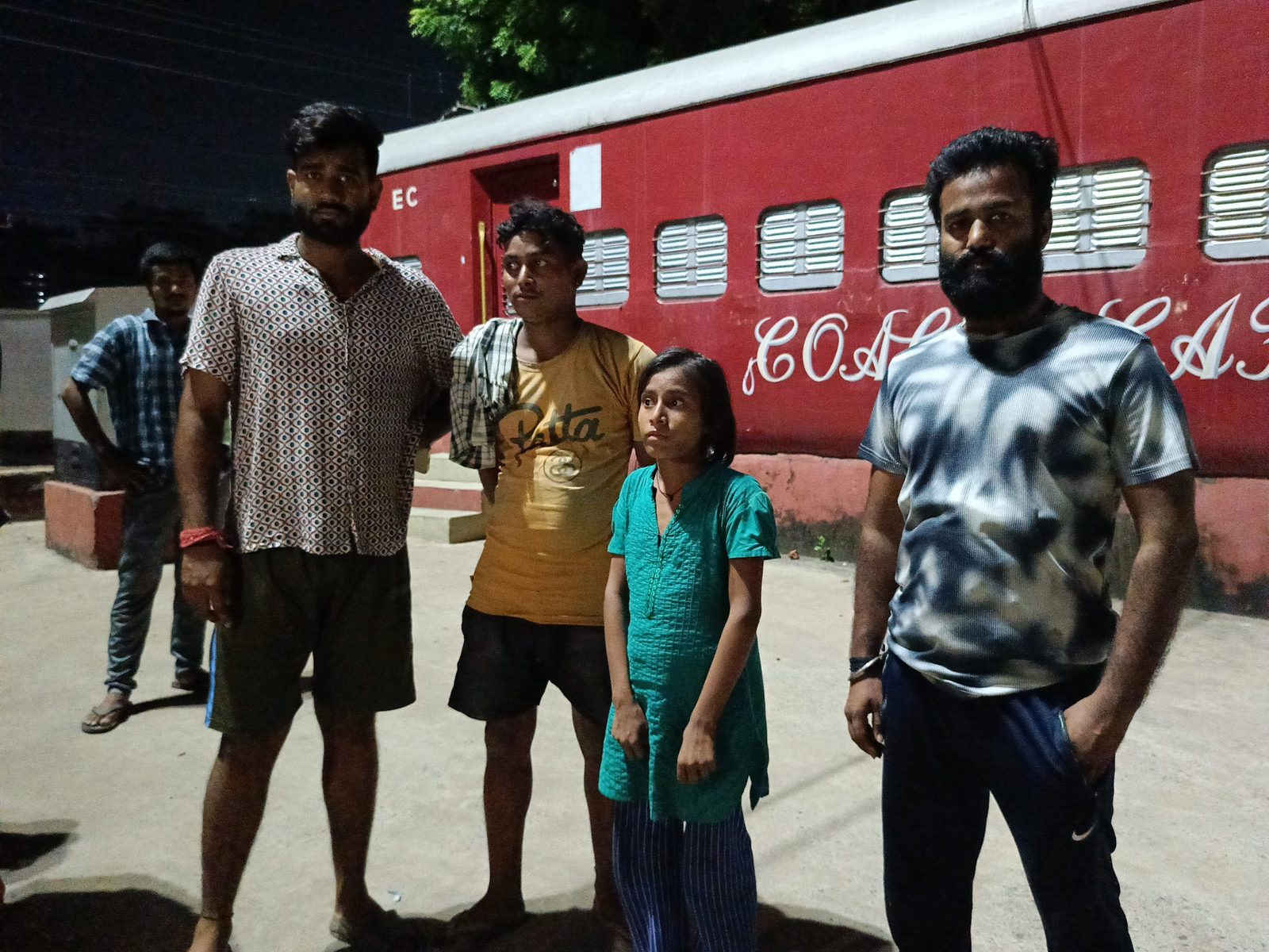 Volunteers with a young girl beside a railway coach at night